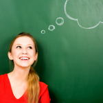 Woman standing in front of blackboard with thought bubbles drawn on it