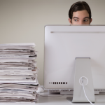 Man sitting at his computer with a pile of documents next to him